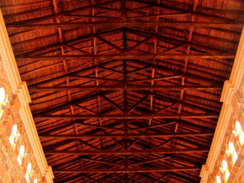 Armadura de vigas de madera bajo el techo del templo de la Inmaculada Concepción, vista desde la nave, sobre los muros de piedra y sus ventanas