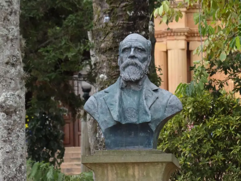 Busto de Aquileo Parra, de barba larga, sobre un pedestal de piedra en el parque principal de Barichara, entre árboles