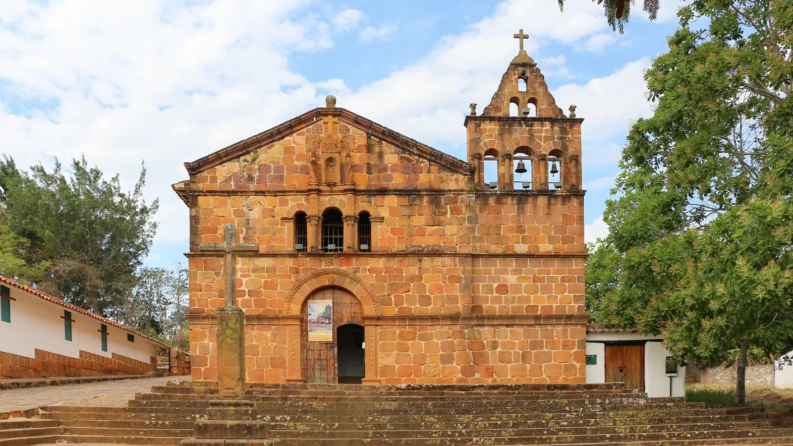 Fachada de piedra de la capilla de Santa Bárbara, con su espadaña de campanas, una cruz de piedra delante y la escalinata, en una foto de enero de 2020