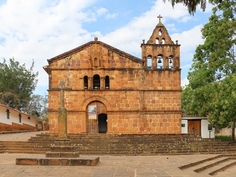 Fachada de piedra de la capilla de Santa Bárbara, con su espadaña de campanas, una cruz de piedra delante y la escalinata, en una foto de enero de 2020