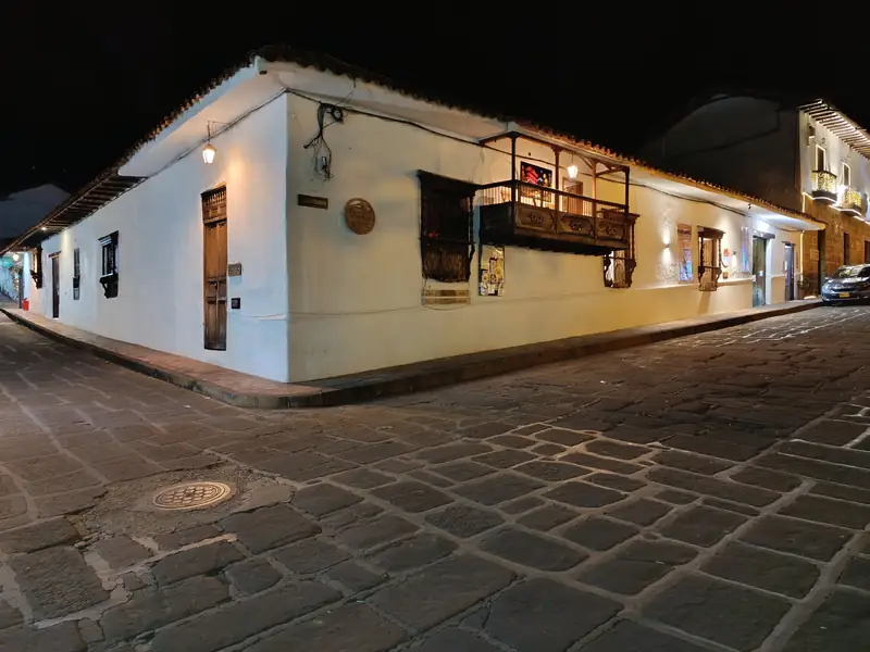 Esquina de la Casa de la Cultura de Barichara de noche: paredes blancas, faroles en el muro, un balcón de madera y la calle de piedra