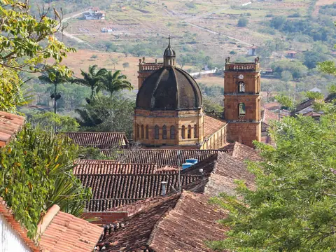La cúpula y las torres del templo asoman sobre techos de teja de barro, entre árboles, con la ladera del valle al fondo