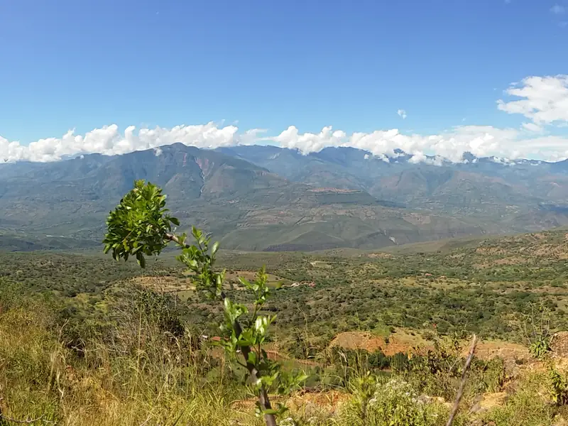 Vista desde el borde occidental de Barichara: el valle con monte seco abajo y, al fondo, una cordillera con nubes blancas bajo el cielo azul