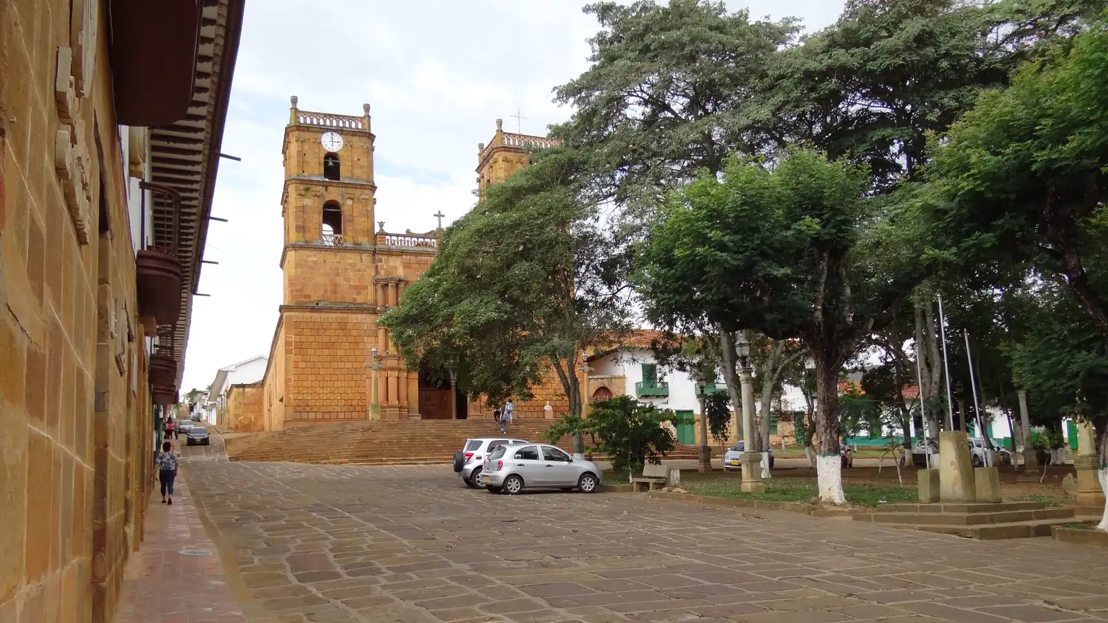 Los árboles del parque principal y, al fondo, el templo de piedra con dos torres en lo alto de su escalinata, junto a una calle de lajas