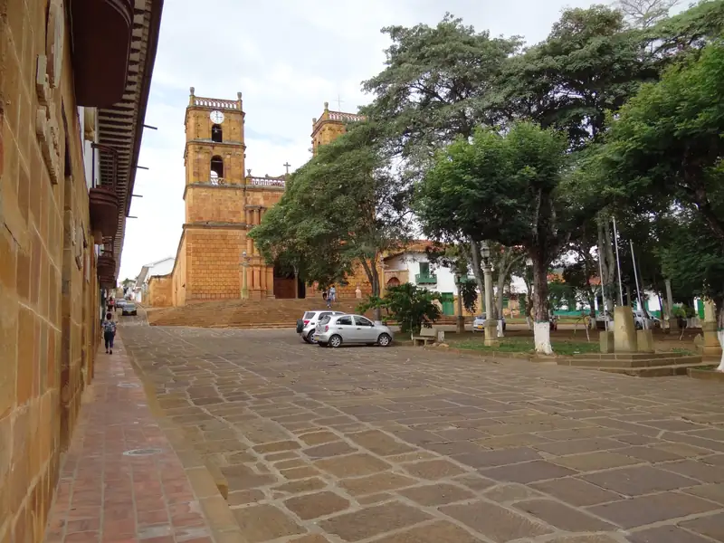 Los árboles del parque principal y, al fondo, el templo de piedra con dos torres en lo alto de su escalinata, junto a una calle de lajas
