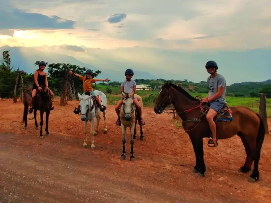 Jinetes con sus caballos en un camino de tierra roja al caer la tarde