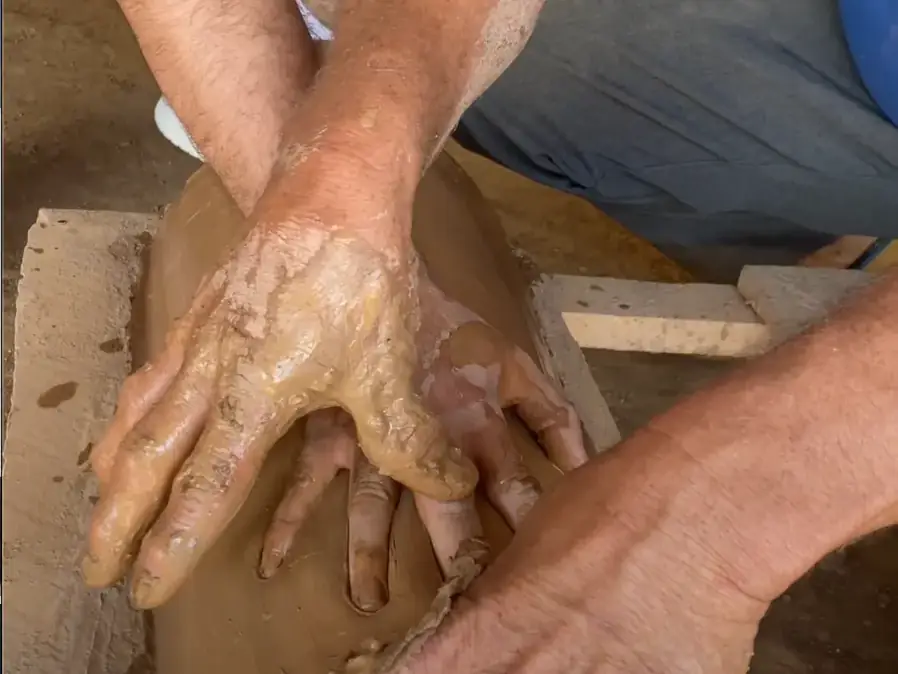 Manos cubiertas de barro dan forma a una teja en el taller