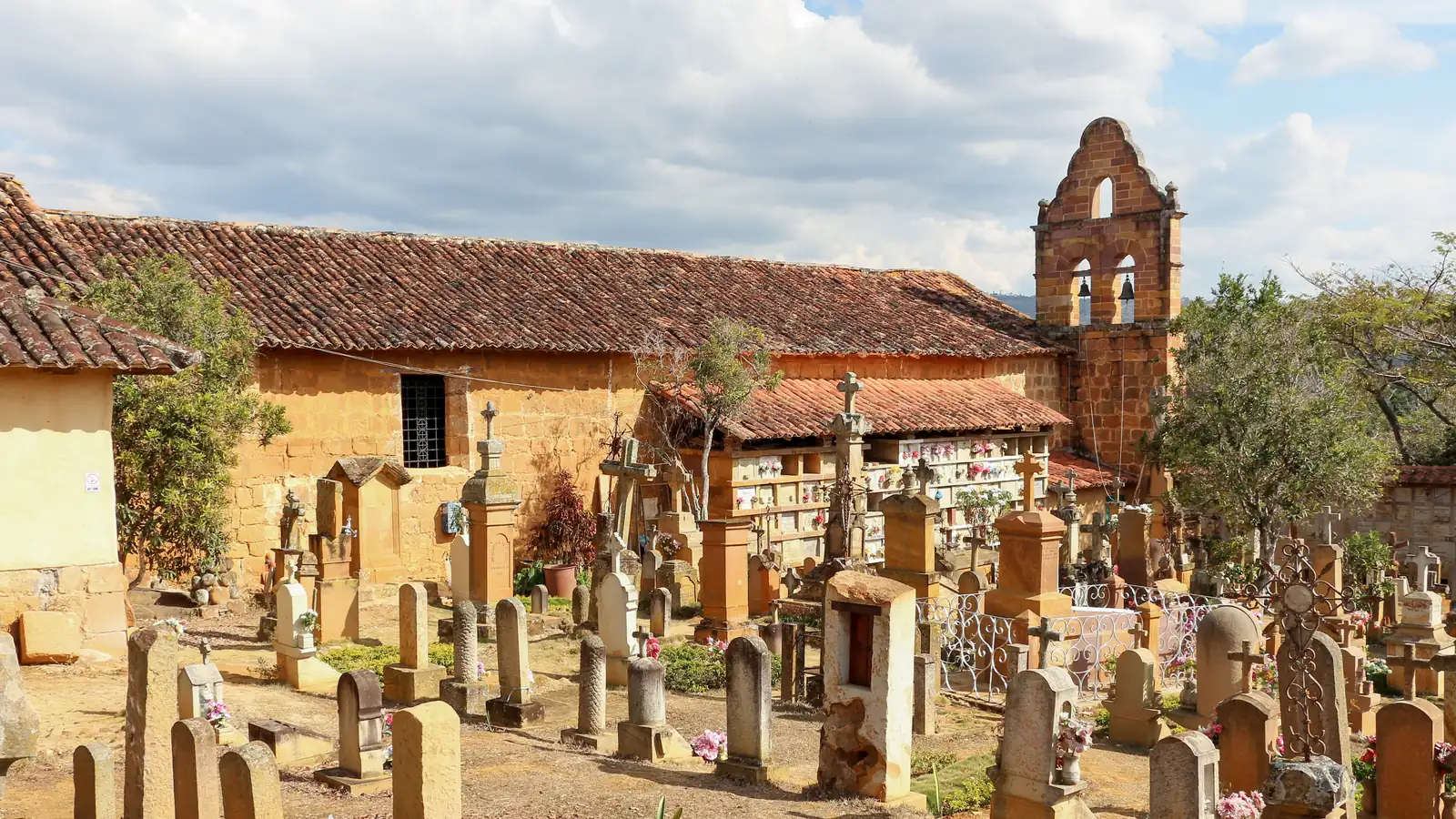 Tumbas, cruces y lápidas talladas en piedra del cementerio, con las bóvedas y el campanario de la Capilla de Jesús detrás