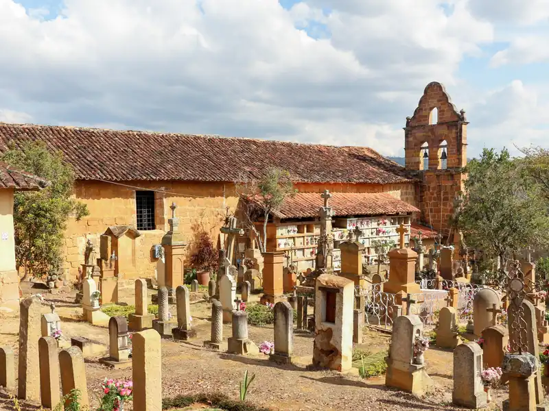 Tumbas, cruces y lápidas talladas en piedra del cementerio, con las bóvedas y el campanario de la Capilla de Jesús detrás