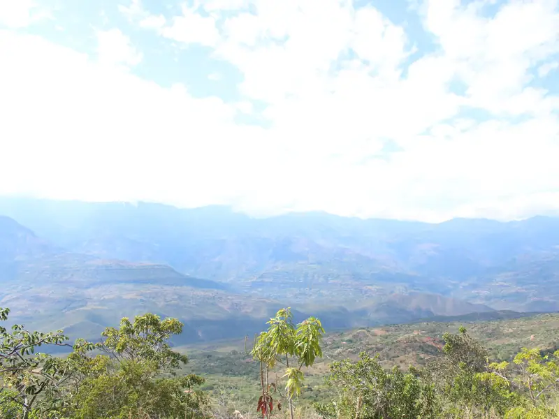 El valle del río Suárez y la serranía al fondo bajo nubes blancas, con árboles y monte bajo en primer plano, visto desde el municipio de Barichara