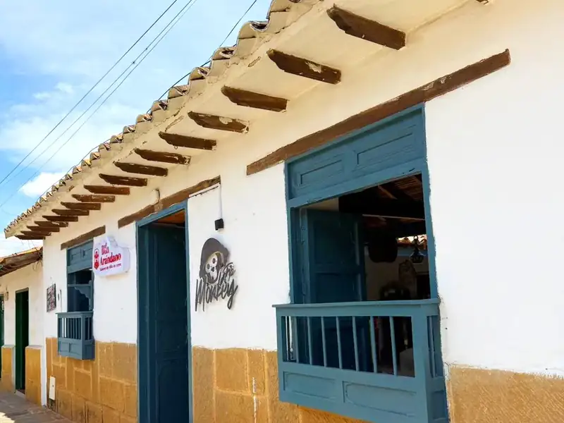 Fachada encalada con ventanas y balcón de madera azul, zócalo de piedra y alero de teja sobre la calle