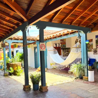 Patio central de la casa colonial, rodeado de columnas azul petróleo y hamacas bajo el alero de teja