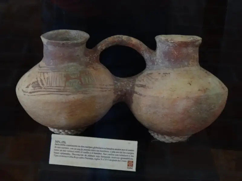 Jarra doble de barro de la cultura guane, con dos cuerpos redondos unidos por un asa y líneas rojas pintadas, en una vitrina