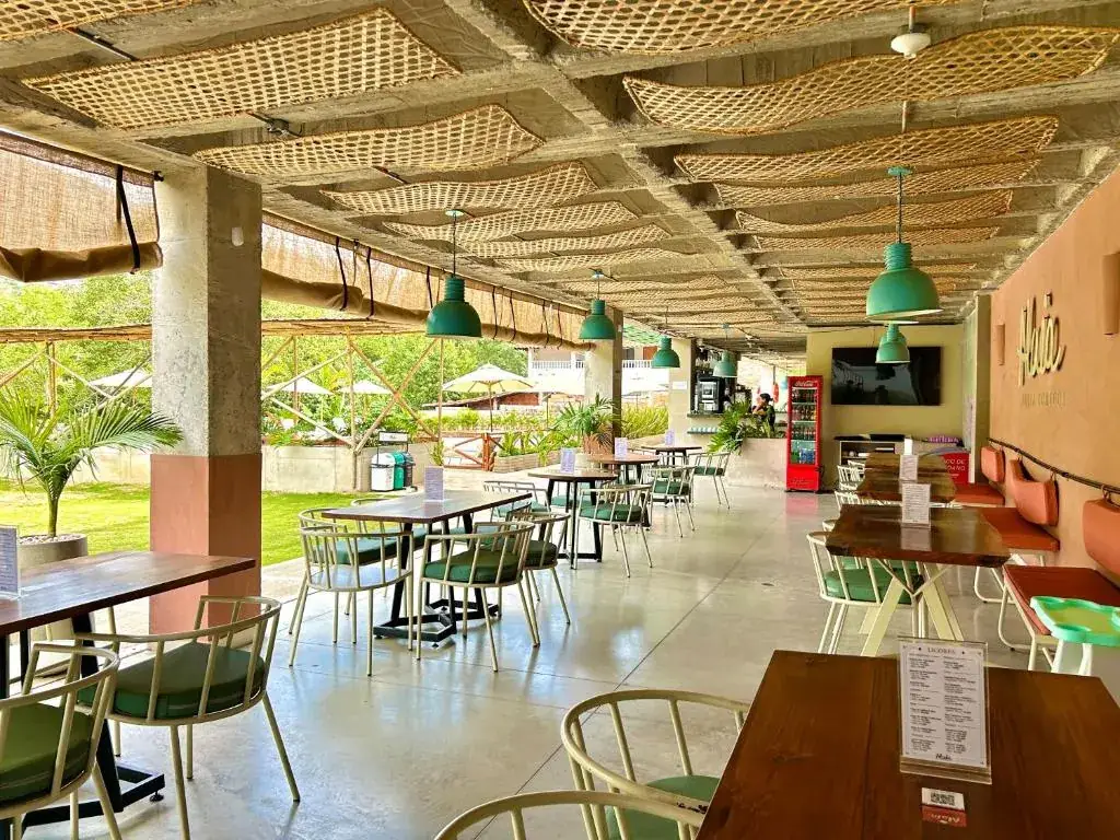 Comedor del restaurante Alaia con techo de esterilla, lámparas verdes y mesas de madera