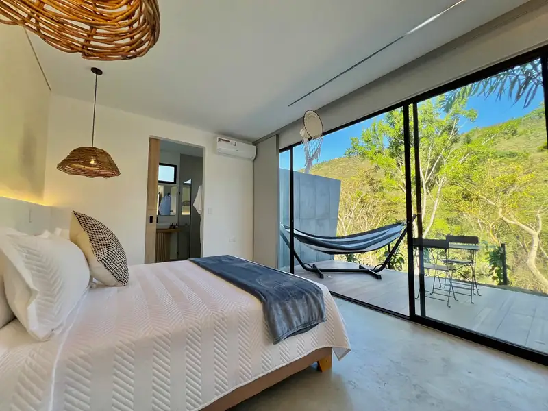 Cama queen del Glamping Deluxe frente al ventanal corredizo, con la hamaca y el jacuzzi del otro lado del vidrio