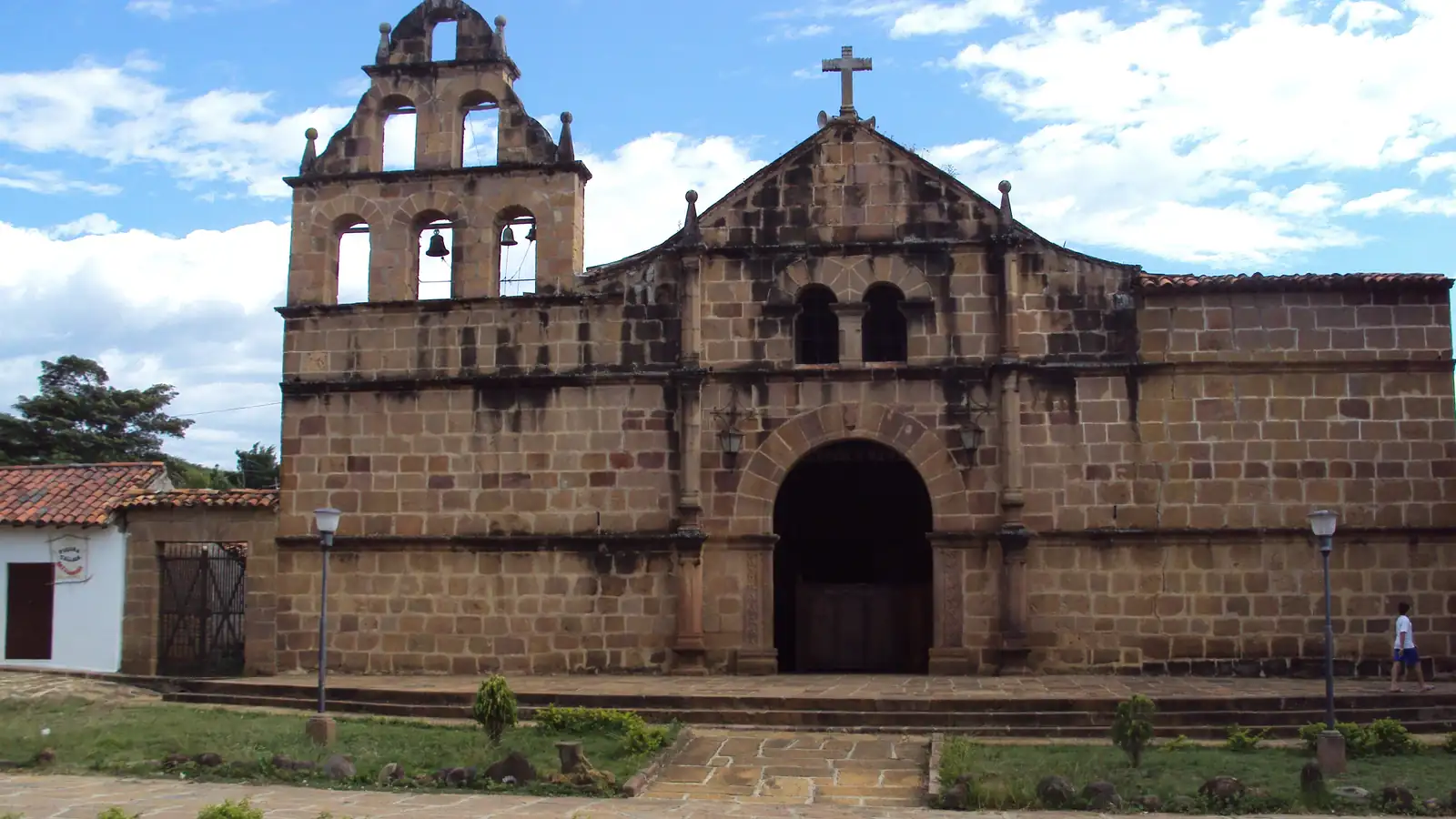 Fachada de piedra de la iglesia de Santa Lucía de Guane, con su espadaña de campanas, una puerta en arco y un jardín delante