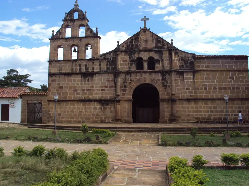 Fachada de piedra de la iglesia de Santa Lucía de Guane, con su espadaña de campanas, una puerta en arco y un jardín delante