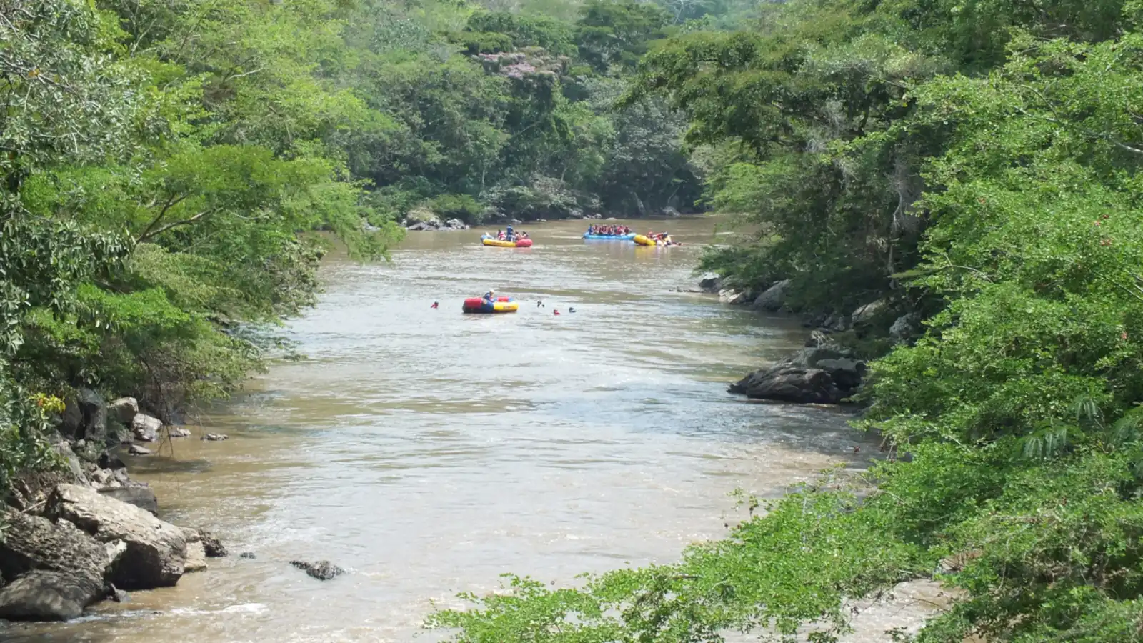 El río Fonce entre árboles y piedras, con balsas de rafting a lo lejos, en San Gil