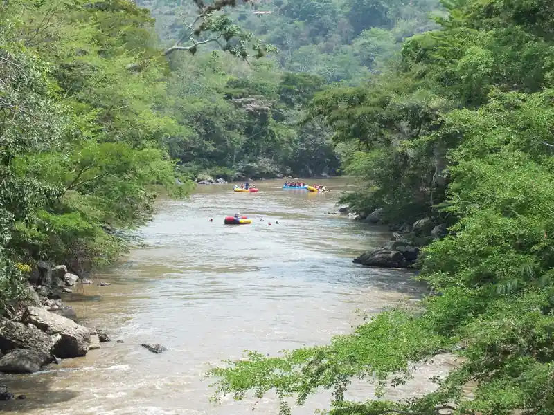 El río Fonce entre árboles y piedras, con balsas de rafting a lo lejos, en San Gil
