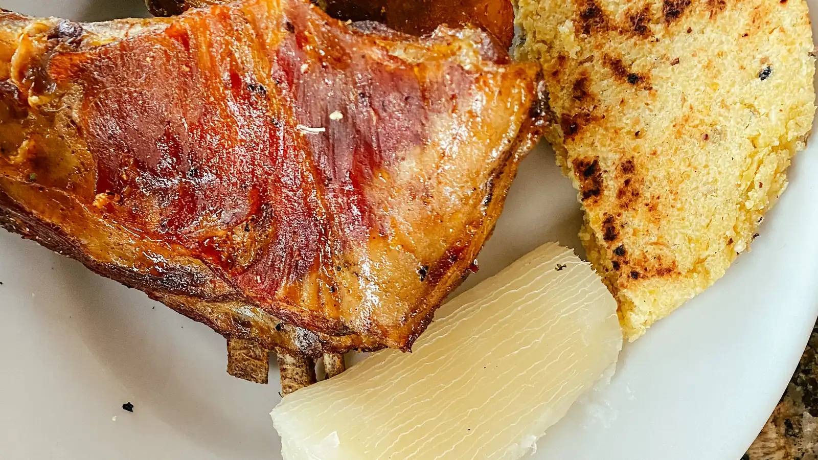 Cabro al horno con un trozo de yuca y una arepa tostada en un plato blanco; al lado, otro plato con pepitoria de arroz