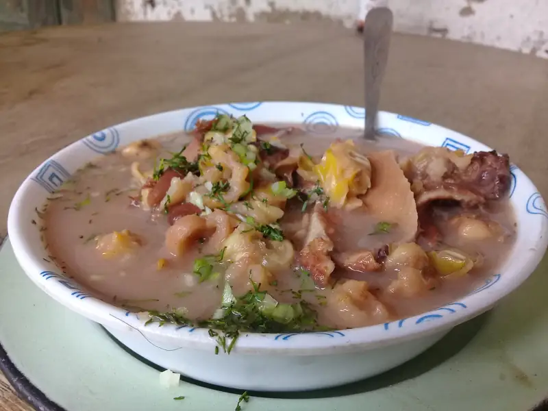 Plato hondo de mute: sopa espesa con maíz pelado, frijol y trozos de carne, con hierbas picadas por encima